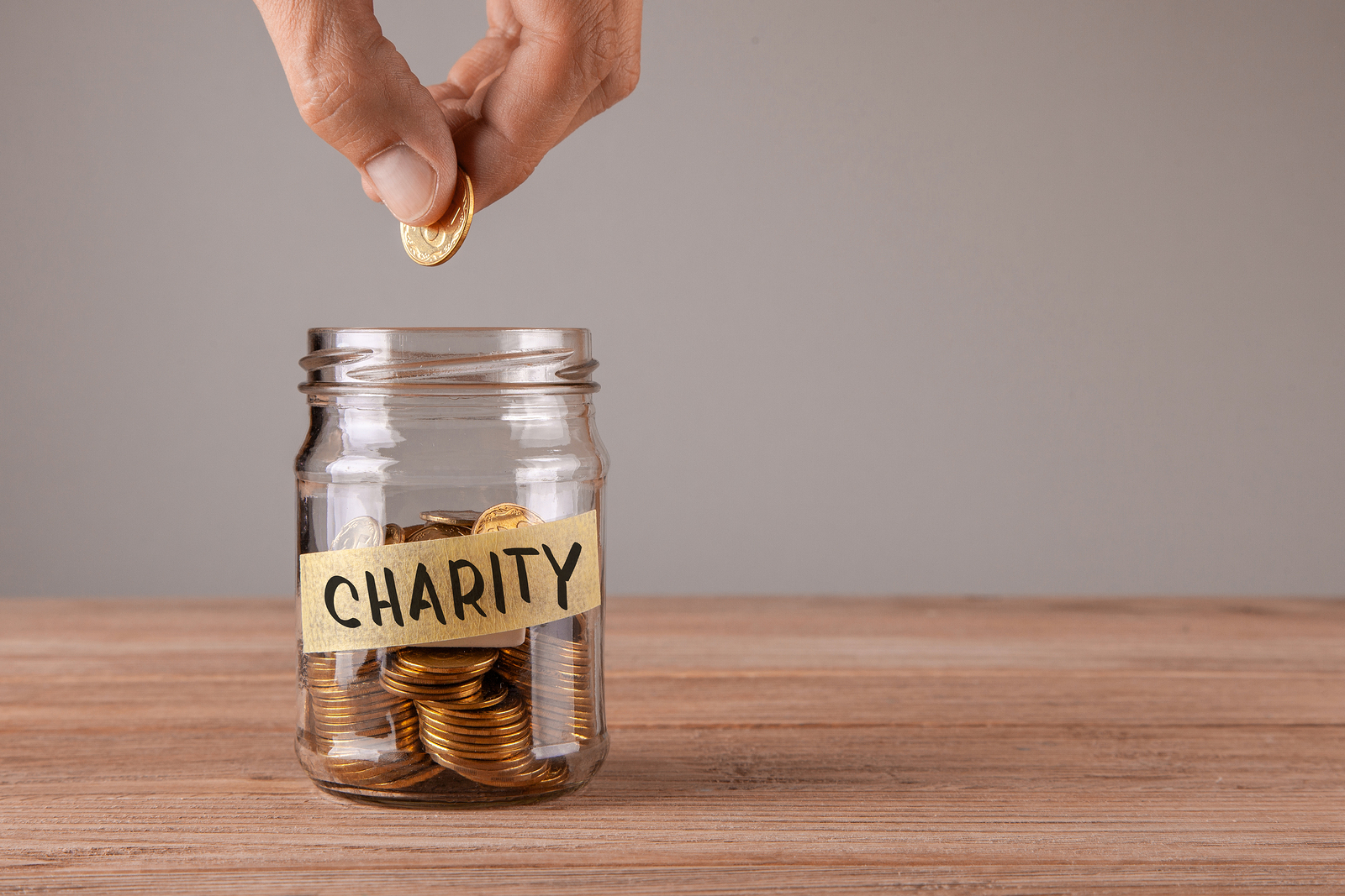 Charity. Glass jar with coins and an inscription charity. Man holds coin in his hand